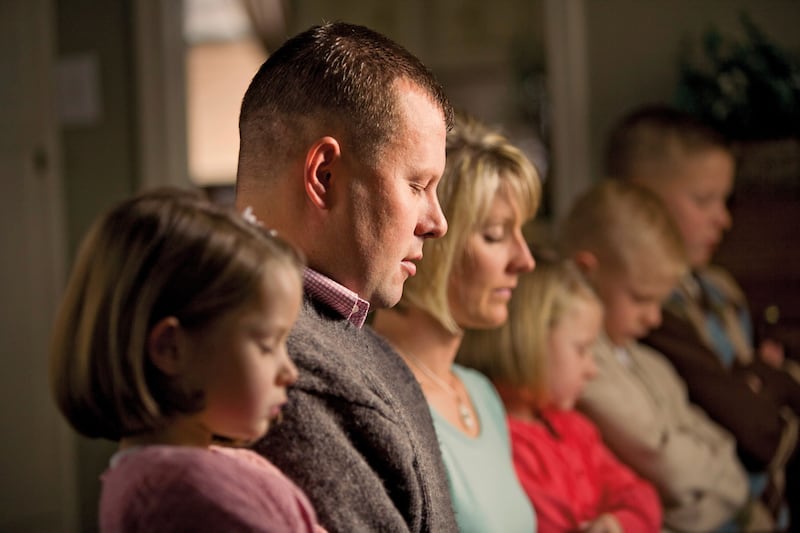 A man and woman and four children bow their heads in prayer.