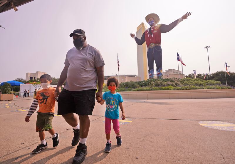 Wearing face masks to prevent the spread of COVD-19, Trey Lipscomb, center, holds the hands of his son, Trey, 6, and daughter Tia, 4, as they walk in front of Big Tex after getting their photo made during a visit to Fair Park in Dallas, Saturday, Sept. 19, 2020. Although the State Fair of Texas was canceled this year, fair organizers are holding drive-thru visits starting this weekend.