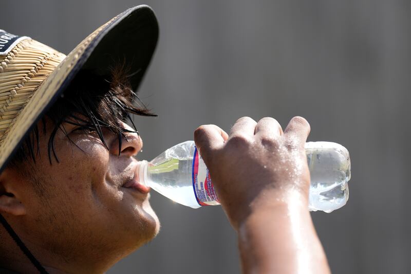 Carlos Rodriguez drinks water while taking a break from digging fence post holes June 27, 2023, in Houston.