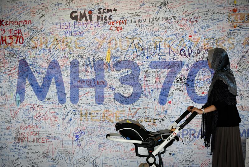 In this 2014 file photo, a woman pushes her baby cart in front of the message board for passengers aboard a missing Malaysia Airlines plane.