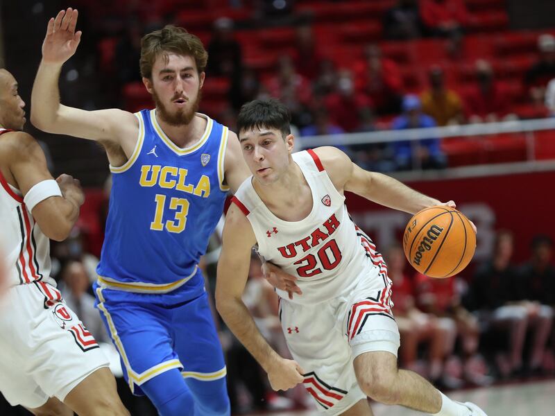 Utah Utes guard Lazar Stefanovic. wearing white, drives on UCLA Bruins guard Jake Kyman
