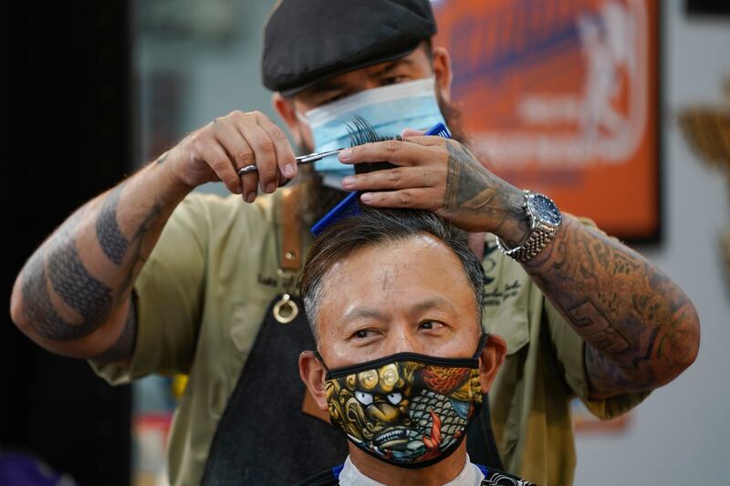 In this May 27, 2020 file photo Luis Lopez wears a face mask while giving a hair cut to Alexander Chin at Orange County Barbers Parlor in Huntington Beach, Calif.