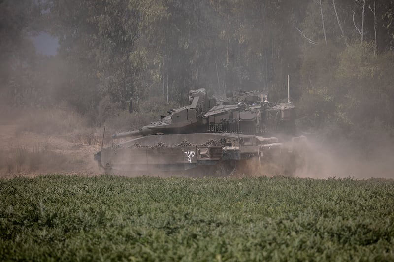 An Israeli tank crosses a road as it advances toward a staging ground near the Israeli Gaza border.