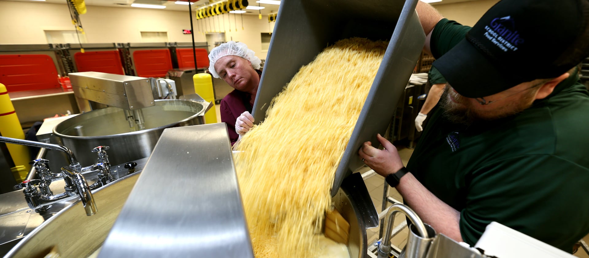 Workers dump cheese into a vat as they make cheese sauce at Bates Central Kitchen in West Valley City, Utah.