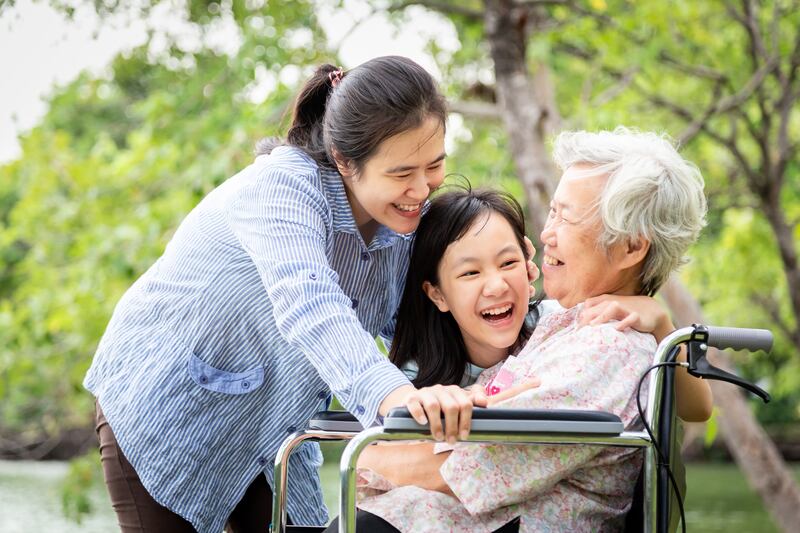 A mother, daughter and grandmother all huddle together outside, laughing.