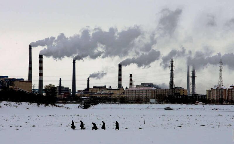 Residents walk across the frozen Songhua River in front of smoke stacks at Jiamusi, in China's northeast Heilongjiang province in this Dec. 4, 2005 file photo. The world's leading climate scientists, in their most powerful language ever used on the issue,