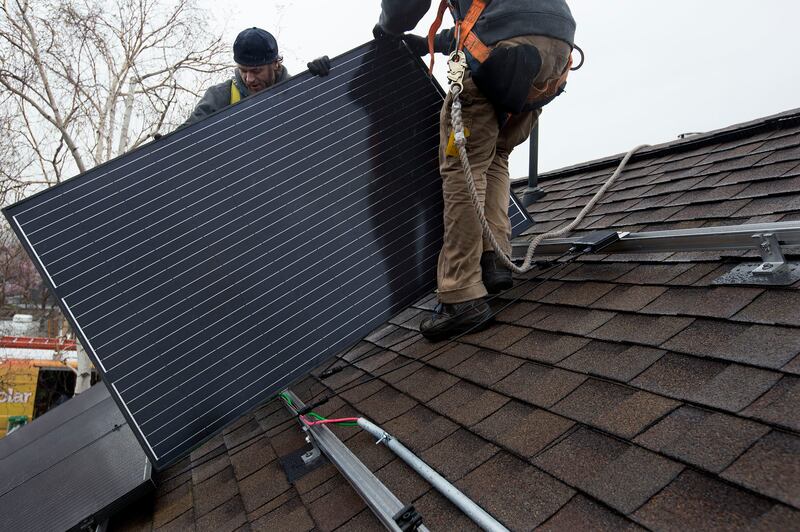 Two men install solar panels on the roof of a home.