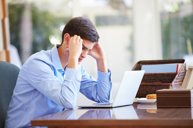 Stressed Teenage Boy Using Laptop On Desk At Home