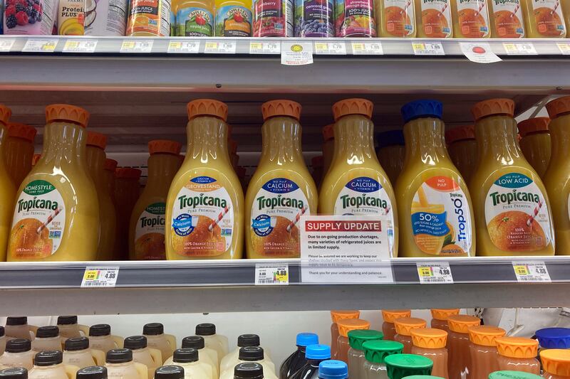 A sign at a grocery store on a shelf of orange juice.
