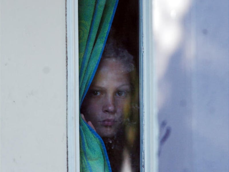 Nicole Coon, sister of Asa Coon, who opened fire at SuccessTech Academy, peers through a window at her home Thursday.