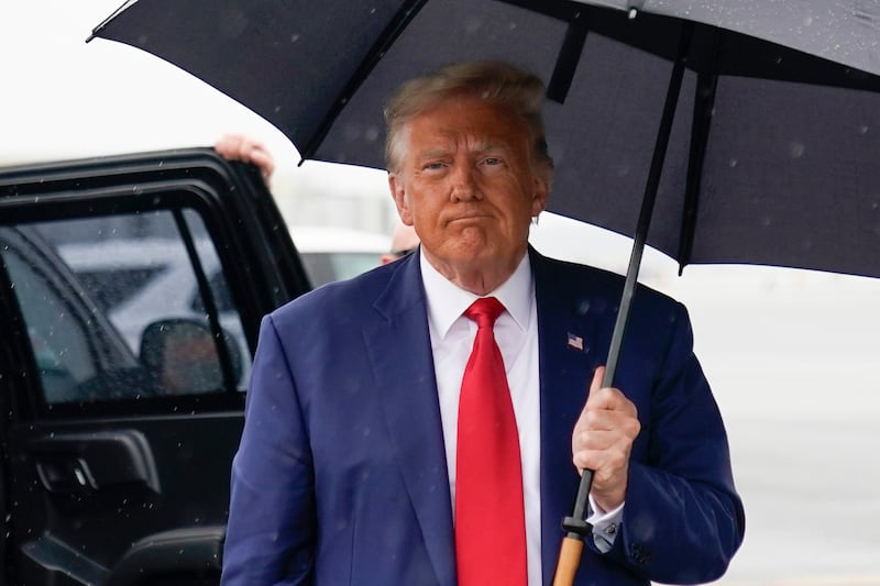 Former President Donald Trump exits a car and holds an umbrella before he boards his plane.