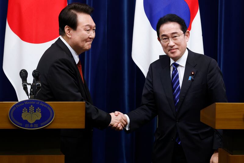 South Korean President Yoon Suk Yeol, left, and Japanese Prime Minister Fumio Kishida, right, shake hands.