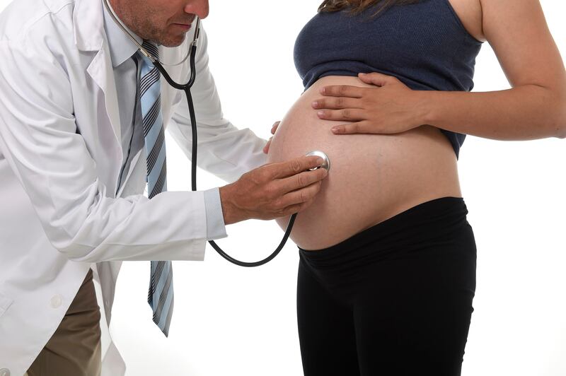 A doctor uses a stethoscope on the stomach of a pregnant woman.