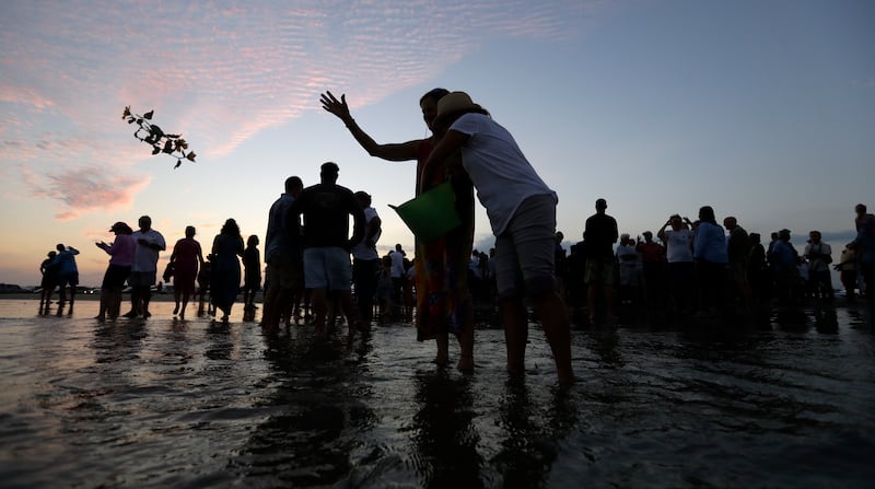 Flowers are tossed in to ocean after a sea turtle with along with the ashes of renowned oceanographer Tony Amos were released into the Gulf of Mexico following a memorial service, Saturday, Sept. 30, 2017, in Port Aransas, Texas. Amos, 80, died of complic