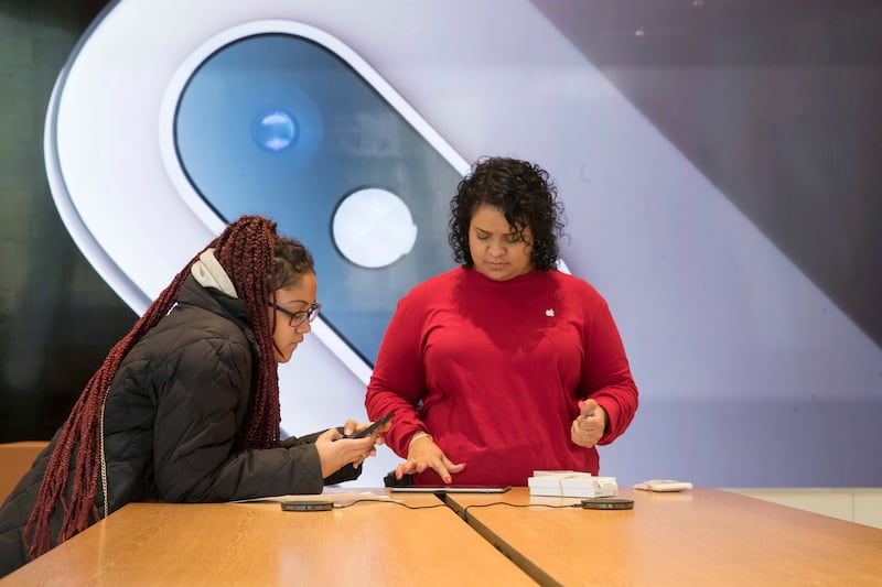 An image of an iPhone is on display in the background as a customer, left, is helped at the Apple store in the Brooklyn borough of New York, Thursday, Jan. 3, 2019.