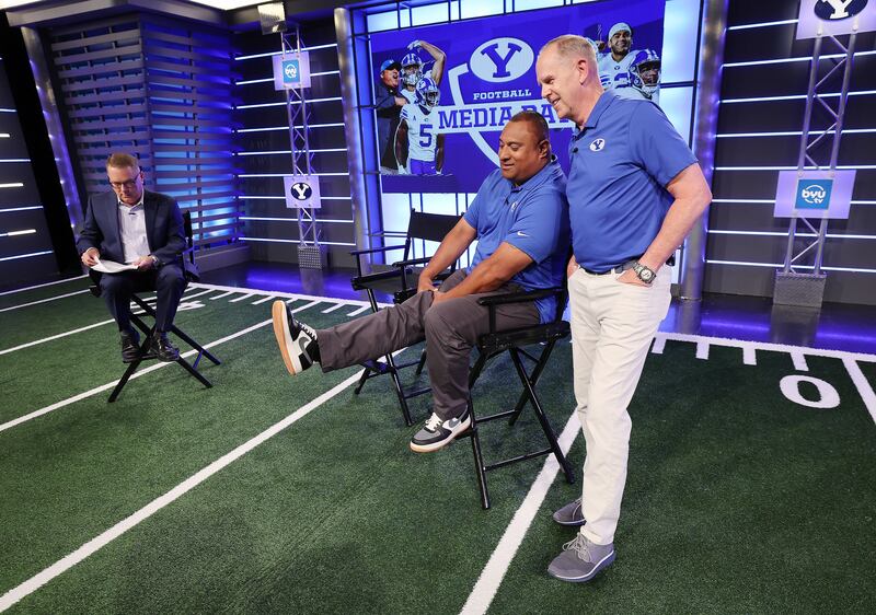 BYU coach Kalani Sitake and athletic director Tom Holmoe stretch during a broadcasting break during BYU football media day.