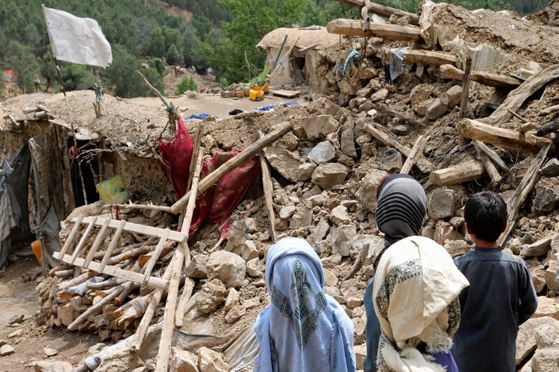 Afghan children stand near a house that was destroyed in an earthquake.