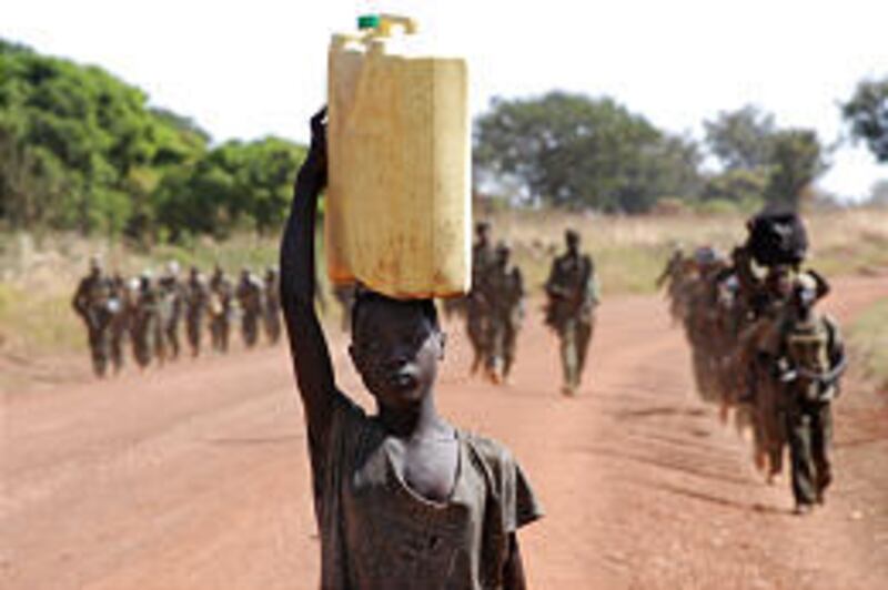 A girl balances a can of water on her head as troops walk in the background in Uganda on Thursday. More than 1.5 million people are forced to take refuge in camps because of rebels.
