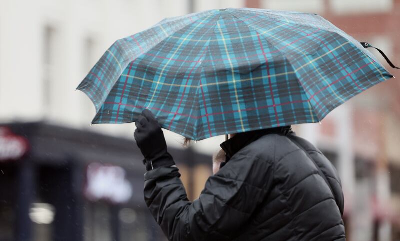 A woman uses her hand to tug on the edge of her umbrella as wind, rain and some snow move into the Salt Lake Valley on Tuesday, Dec. 27, 2022.