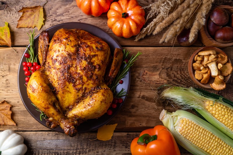 A cooked chicken sits on a table surrounded by autumn vegetables.
