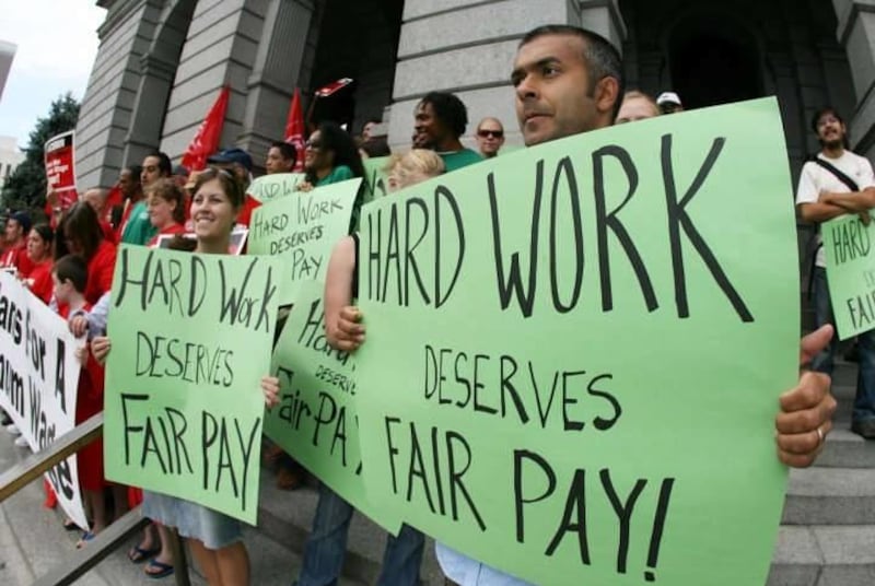 Kirpal Singh of Denver, right, waves a placard along with more than 100 other supporters of raising the minimum wage in Colorado during a rally on the steps of the state Capitol in Denver this past summer.