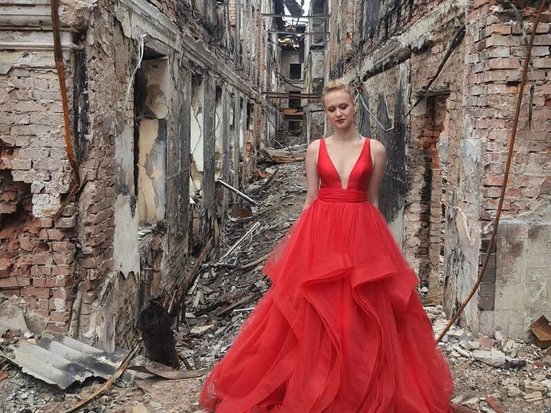 A woman identified as a high school graduate named Valerie is pictured in front of her destroyed school in Ukraine.