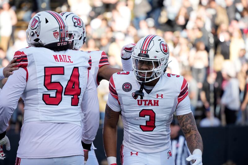 Utah quarterback Ja’Quinden Jackson, wearing white, is congratulated by offensive lineman Paul Maile
