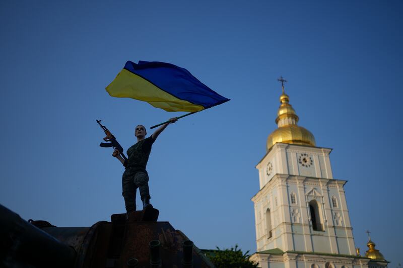 A woman brandishes a Ukrainian flag standing on top of a destroyed Russian tank in Kyiv, Ukraine.