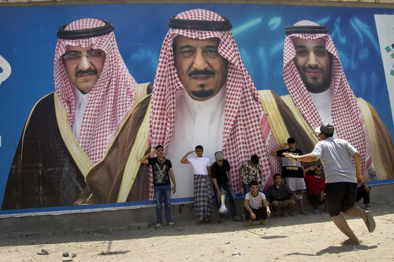 FILE - In this April 4, 2017, file picture Saudi boys pose in front of a huge billboard showing in the center, King Salman, with his 31-year-old son Mohammed bin Salman to the right, and Prince Mohammed bin Nayef to the left in Taif, Saudi Arabia. Salman
