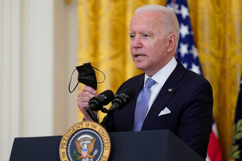 President Joe Biden holds a face mask as he makes an announcement from the East Room of the White House.