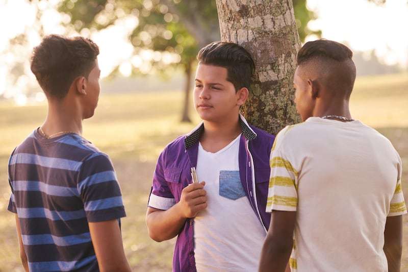 A group of three teenage boys with an e-cigarette.