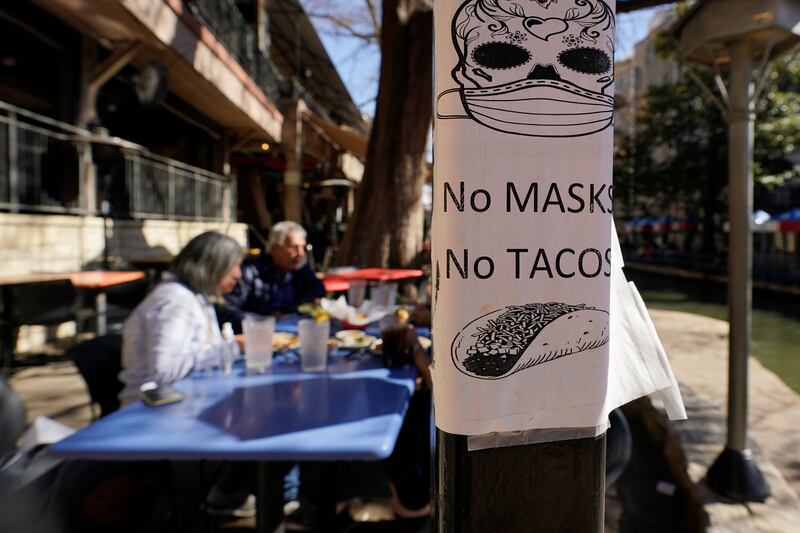 A sign requiring make is seen near diners eating at a restaurant on the River Walk, Wednesday, March 3, 2021, in San Antonio. Gov. Greg Abbott says Texas is lifting a mask mandate and lifting business capacity limits next week.