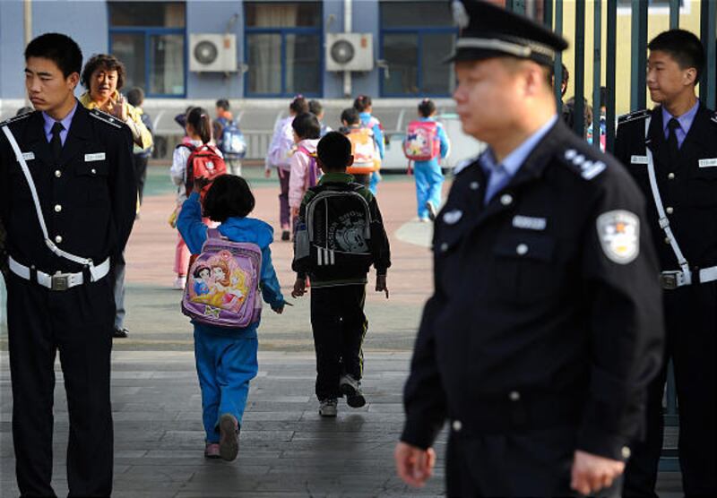 A student waves to her teacher while walking past security officers and a policeman standing guard outside an elementary school in Beijing on Tuesday. Parents dropped off their children on the first day of classes after three attacks last week.