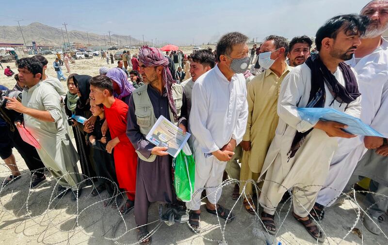 A man holds a certificate acknowledging his work for Americans as people gather outside the airport in Kabul, Afghanistan
