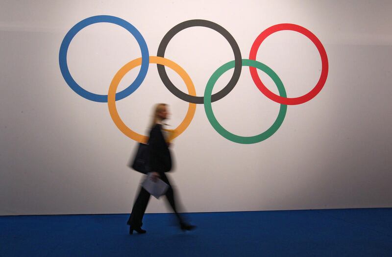 A woman walks in front of a board showing Olympics rings at the 127th International Olympic Committee session in Monaco, Monday, Dec. 8, 2014. Athletes from Kosovo will be able to compete at the 2016 Summer Games after being granted full recognition on Tu