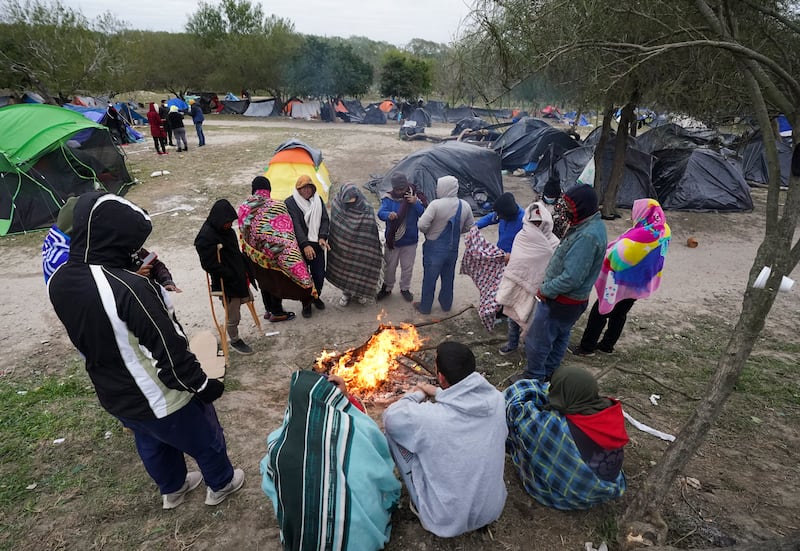 Migrants stand in the cold weather around a campfire at a makeshift camp on the U.S.-Mexico border on Dec. 23, 2022.