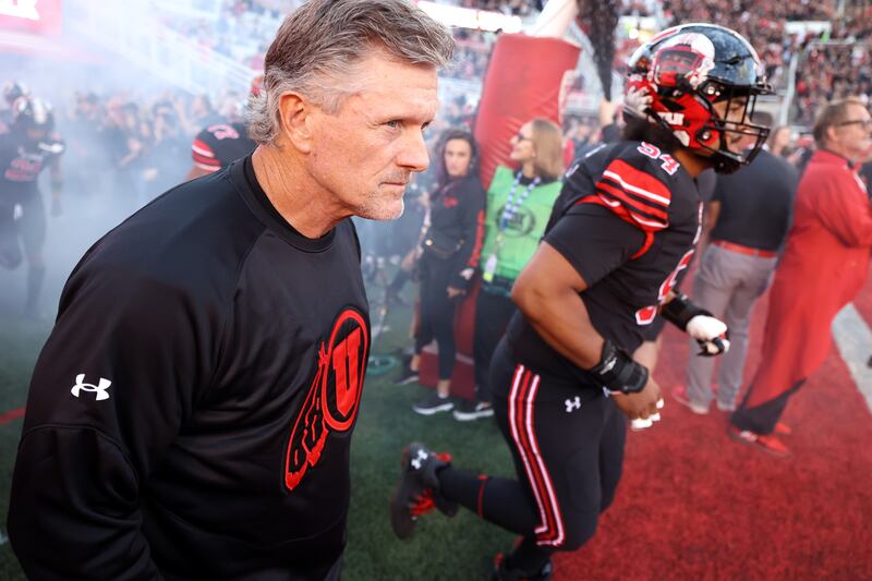 Utah Utes head coach Kyle Whittingham, wearing black, runs out with his team.