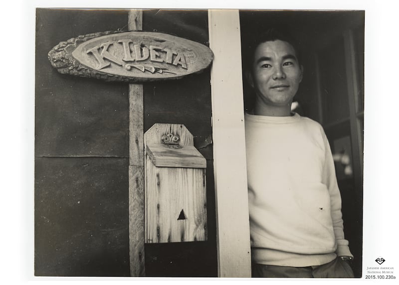 Photo from the Allen Hendershott Eaton Collection. Caption on back reads "Door nameplate of Kitaro Ideta. In doorway is son Takashi Ideta who was on furlough from army service. Photograph by Paul Faris." This photo was taken at the Jerome War Relocation C