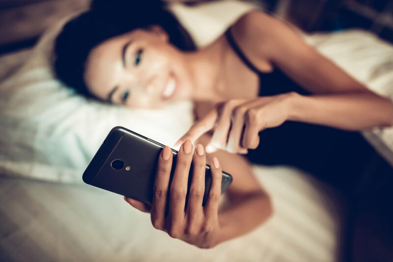A woman uses a smartphone while lying in bed.