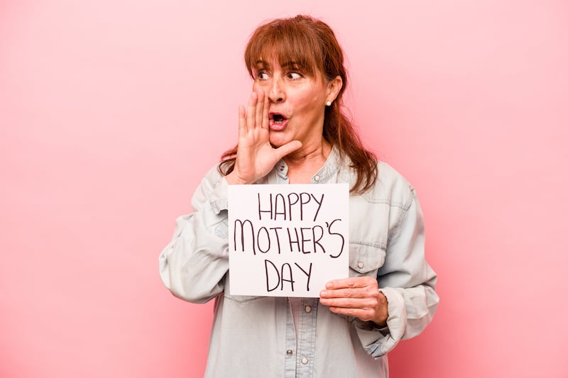 Middle-aged woman holds a sign that says “Happy Mother’s Day” while holding a hand to her mouth and speaking advice.