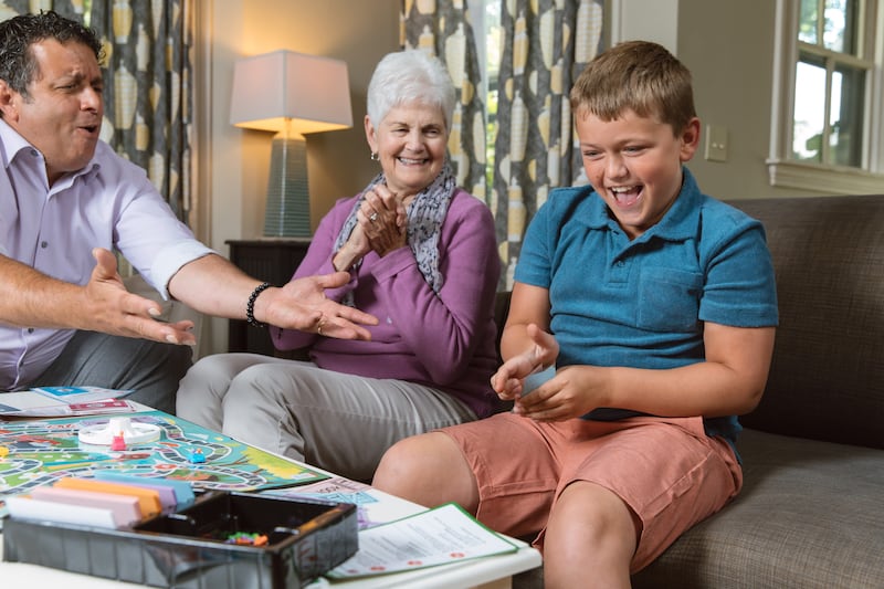 A boy plays a board game with a man and an older woman.