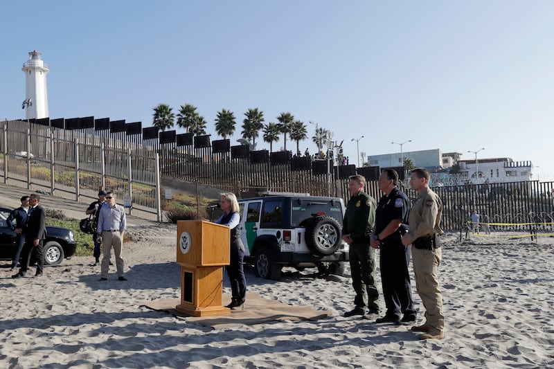 Secretary of Homeland Security Kirstjen Nielsen, center at podium, speaks in front of the border wall separating Tijuana, Mexico, behind, and San Diego, Tuesday, Nov. 20, 2018, in San Diego. Nielsen said Tuesday an appeal will be filed on the decision by