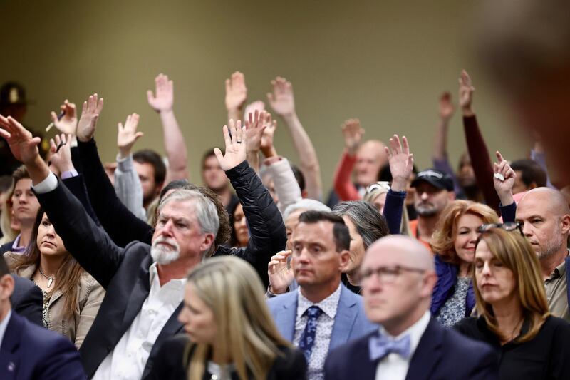 People opposed to the Biden administration’s vaccine mandate raise their hands in Utah hearing.