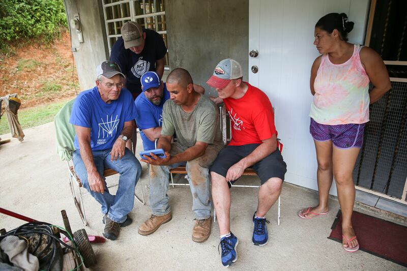José Antonio Vera Ortiz, center, shows photos of the aftermath of Hurricane Maria to Al Dustin, Statton Davis, Ben Davis and Dan Dustin, left to right, while Ortiz's wife, Darissa Romàn Frontera,  looks on at their home in Las Marías, Puerto Rico, on Sund