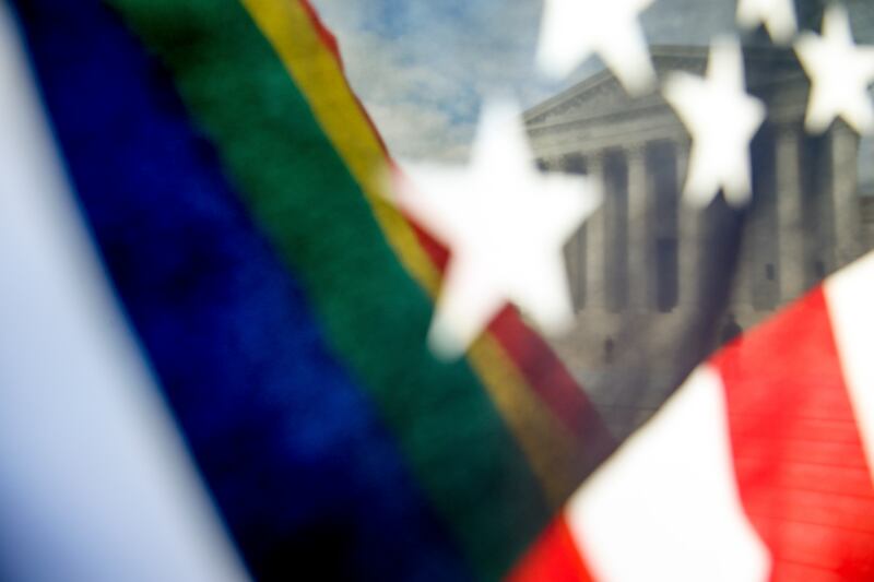 A rainbow colored flag, seen through an American flag, flies in front of the Supreme Court in Washington.