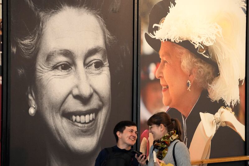People walk out of an exhibition past Queen Elizabeth II posters at Buckingham Palace in London on Thursday, Sept. 8, 2022.