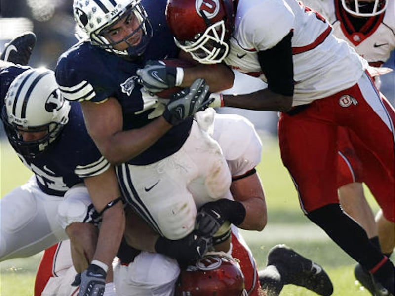 BYU's Harvey Unga slams into Utah's Stevenson Sylvester, bottom, and Robert Johnson, right.