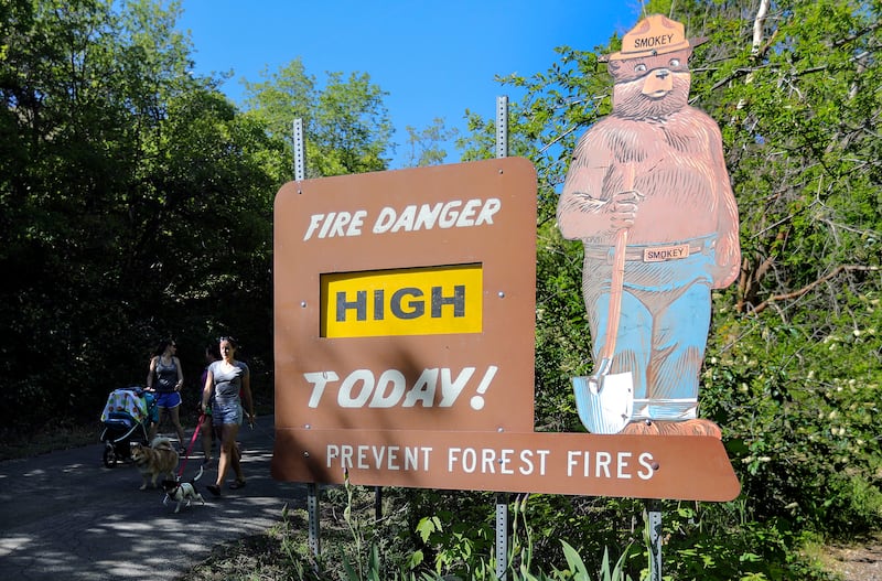 A fire danger sign is shown reading “High” in City Creek Canyon in Salt Lake City as two people walk by.