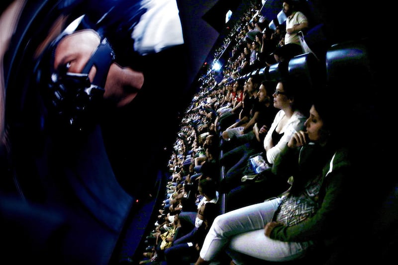 In this photo taken with a fisheye lens, people watch villain Bane on the screen during the midnight premiere of "The Dark Knight Rises" inside the Liberty Science Center IMAX theater Friday, July 20, 2012, in Jersey City, N.J. A gunman in a gas mask barg