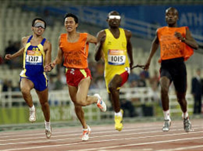 Blind Chinese runner Xiang Wu, left, is led by a guide as he holds off Angola's Jose Armando during the 100 meter in Athens Tuesday.